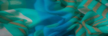 Bulanık mavi ve yeşil kumaş yumuşak dalgalarda altın çizgilerle vurgulanır ve modern tekstil sanatını yansıtan zengin bir doku yaratır..