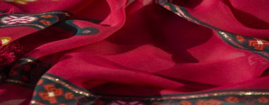 Bulanık efekt, turuncu çiçek desenleri ve koyu yeşil kenarlı koyu kırmızı kumaşı artırarak görsel olarak çarpıcı bir tekstil parçası oluşturur..