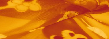 Bulanık turuncu kumaş, narin çiçek desenleri, yumuşak ışık altında aydınlatılmış, şeffaf katmanlarını ve desenlerin ve gölgelerin sanatsal etkileşimini sergiliyor..