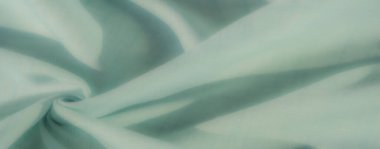 Yumuşak pastel yeşil kumaştan bulanık. Karmaşık kıvrımlar, hafif ışıklandırmayla vurgulanmış zayıf ızgara desenleri, canlandırıcı bir görsel estetik sunuyor..