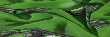 Canlı yeşil kumaş bulanıklığı. Mor, beyaz, çiçek desenleri ve geometrik tasarımlar. Yumuşak püsküller kumaşa karmaşık ve dekoratif bir dokunuş ekler..