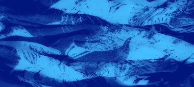 Bulanık, ince mavi kumaşı, karmaşık beyaz çiçekli desenleri ve görünür dokusuyla yakına çeker. Yumuşak, soyut bir estetik sunar..