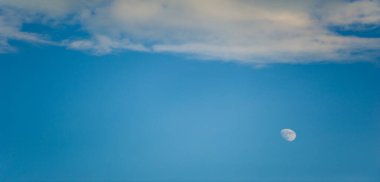 Sakin mavi bir arkaplan karşısında tüylü, beyaz bulutlarla dolu engin bir gökyüzü manzarası. Barışçıl atmosfer yumuşak şekiller ve bulutların dinamik hareketleriyle vurgulanır..
