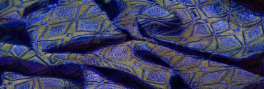 Mavi ve altın renginde parıldayan kumaş. Geometrik elmas desenli. Moda, dekor ya da yaratıcı arka planlar için zarafet ve canlılık yayıyor..