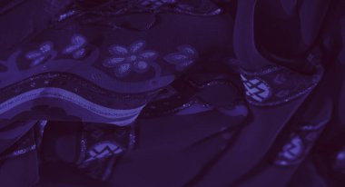 Simetrik desenler ve parıldayan aksanlarla bezenmiş, sofistike ve sanatsal incelik hissi uyandıran zengin mor bir kumaşın bulanık görüntüsü..