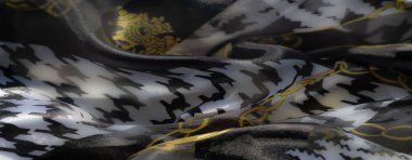 Altın zincir motifleriyle süslenmiş saydam siyah ve beyaz kumaşın karmaşık etkileşimi lüks ve dinamik bir estetik yaratıyor..