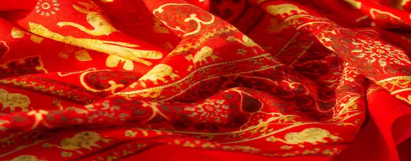 Görüntü, altın fil motifleri ve desenleriyle süslenmiş zarif bir kırmızı tekstil sunar. Kültürel zenginliği ve karmaşık işçiliği vurgular..
