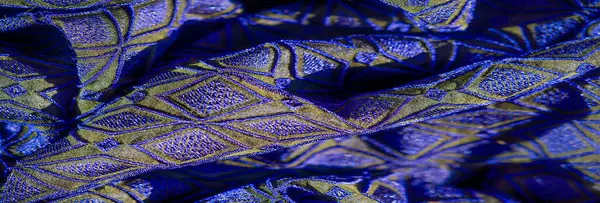 Geometrik elmas desenleri ve parıldayan dokusu olan parlak mavi ve altın renkli bulanık kumaş yaratıcı tasarımlar için lüks ve göz alıcı bir zemin oluşturuyor.