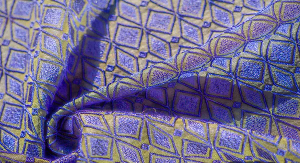 Bulanık, karmaşık geometrik nakış, mavi ve altın rengi. Kumaşın parıldayan dokusu zengin tasarımına cesur ve lüks bir estetik katıyor..