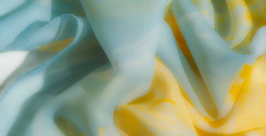 Bulanık sarı ve mavi kumaş kıvrımları hareketli bir dokuya sahiptir, akışkan desenli sanatsal bir cazibe yayar ve ışık ve gölgenin sakin etkileşimi