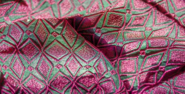 Karmaşık geometrik pembe nakışlı yeşil bir kumaşın bulanık görüntüsü pürüzsüz kıvrımlar ve lüks bir doku sergiliyor. Canlı tasarım, kumaşın dinamik ve sofistike yapısını geliştirir.