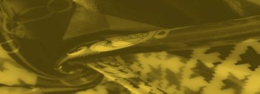 Birbirine kenetlenmiş zincir desenleri ve geometrik motiflerle bulanık sarı kumaş yaratıcı projelerde kullanım için mükemmel, zengin, dokulu bir tasarım yaratıyor..