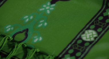 Görsel zenginlik için pürüzsüz bir doku ve dekoratif püsküllerle vurgulanmış, karmaşık geometrik ve çiçek desenli, canlı yeşil kumaş kıvrımları..