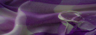 Yumuşak mor ve krem kumaşın bulanık, yarı şeffaf, ışıldayan bir yüzeyi var, canlı mor aksanlar ve dinamik bir doku için gevşek ipliklerle süslenmiş..