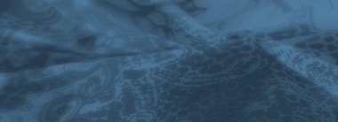 Görüntü. Kapalı mavi tonlarda karmaşık çiçek desenleri içeren katlanmış bir kumaş. Tekstil sanatının karmaşıklığını vurguluyor..