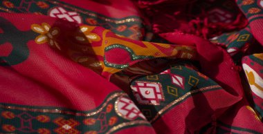 Canlı sarı, turuncu ve yeşil tonlarda çiçekli ve geometrik tasarımlı bulanık kırmızı kumaş. Yumuşak dokular ve karmaşık desenler bu tekstili görsel olarak çarpıcı kılıyor..