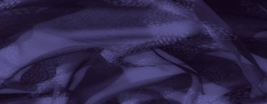 Görüntü. Koyu mor kumaştan büyüleyici bir yakın plan, kıvrımları ve çiçeklerden esinlenilmiş desenleri yumuşak ışıkta yakalıyor. Karmaşık tasarım ve gölge oyunu derinlik ekler