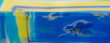 Bulanık mavi kumaş yumuşak sarı ve beyaz çiçek desenleriyle süslenmiş. Yumuşak kıvrımlar kumaşların hafif ve havadar dokusunu güçlendirir. Zarif ve kaprisli bir cazibe yaratır..