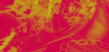 Görüntü. Pürüzsüz ve zarif şekillerde katlanmış, zincir motiflerle birbirine dolanmış, karmaşık çiçek ve geometrik desenler gösteren canlı sarı ve kırmızı bir kumaş..