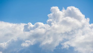 Parlak mavi gökyüzüne karşı dramatik beyaz bulutlar gösteren canlı bir fotoğraf ihtişam hissi yaratıyor bulutların zengin dokusu manzarayı dolduruyor, açık havanın güzelliğini vurguluyor.