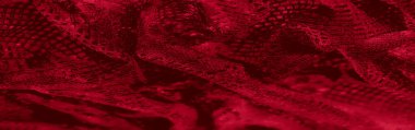 Karmaşık dokuma ve kalın desenlerle kırmızı dokuma dokusunun bulanık detayları. Dinamik kıvrımlar ve zengin renkler lüks ve sanatsal cazibe yayar..