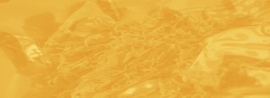 Süslü çiçek motifleri ve simetrik geometrik tasarımlar içeren bulanık sarı kumaş, ince bir parıltı ve parlak bir görünüş ile vurgulanmış..