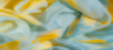 Yumuşak, pürüzsüz kıvrımları olan akışkan sarı ve açık mavi kumaşın bulanık görüntüsü dinamik soyut bir tasarım ve canlı dokular etkileşimi sergiliyor..