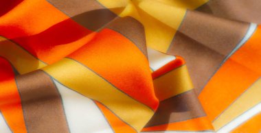 Kahverengi, sarı ve turuncu çizgilerden oluşan kıvrımlı, saten benzeri kumaş üzerinde bulanık bir etki. Her renk ince, ince mavi çizgilerle ayrılmış, samimi ve davetkar bir görünüm yaratıyor..