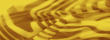 Koyu kahverengi kıvrımlarla zenginleştirilmiş sarı kumaşın bulanık görüntüsü. Canlı tonların ve akışkan kıvrımların etkileşimi canlı ve görsel bir kompozisyon oluşturur..