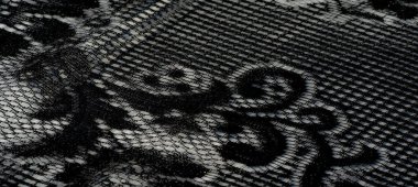 Zarif desenleri olan lüks siyah dantelli kumaş bulanıklığı ışıkla parıldıyor ve ince kıvrımları ve dokularıyla zarif bir görsel etki yaratıyor..