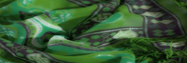 Bulanık: Karmaşık mor desenli ve hassas kenarlı yeşil kumaşın dinamik bir görüntüsü, dokunun ve canlı renklerin uyumunu gösteriyor.