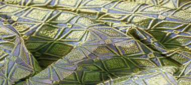 Altın aksanlı, katlanmış yeşil ve mavi kumaşın bulanık görüntüsü. Elmas şekilleri görsel olarak dinamik ve dokulu bir desen oluşturur..