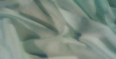 Pürüzsüz pastel yeşil kumaşın kıvrımları ve ince ışıklandırmasıyla bulanıklaşır. Yumuşak malzeme zarafet ve sakinlik yayar, modern, minimalist tasarımlar için mükemmeldir..