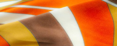 Turuncu, sarı ve kahverengi renkli, ince mavi çizgi aksanlı katlanmış kumaş üzerinde bulanık bir etki. Kumaşın pürüzsüz dokusu ve sıcak tonları samimi ve davetkar bir his katar..