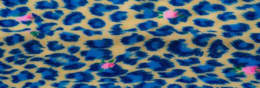 Bej arka planda pembe çiçek aksanlı canlı mavi leopar benzeri yumuşak kumaş sergilenen bulanık yakın plan. Karmaşık dokusu, canlı ama yumuşak bir estetik katıyor..