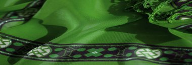 Siyah ve beyaz tonlarında koyu çiçekli ve soyut desenli yeşil bir kumaşa yakın plan, akışkan püsküller ve yumuşak gölgelerle vurgulanmış..