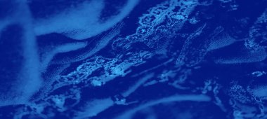 Pürüzsüz kıvrımlar ve zarif tasarımda yansıtıcı gölgeler gösteren, karmaşık dokular ve desenler içeren canlı mavi kumaştan oluşan bulanık bir makro.