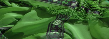 Karmaşık desenli ve örgülü yeşil kumaşların bulanık görüntüsü. Tasarım, soyut geometrik şekiller ve hassas dokularla canlı renkler sergiler..