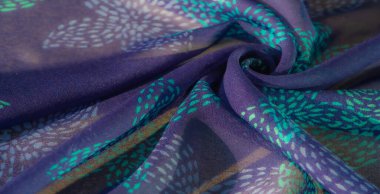 Turkuaz ve deniz mavisi lekeli mor kumaş yakın plan, büyüleyici bir desen oluşturuyor. Kumaşın havadar dokusu ve pürüzsüz kıvrımları rahatlatıcı bir görsel etki yaratır..