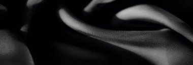 Yumuşak, katmanlı kıvrımları ve pürüzsüz, gölgeli dokusu olan siyah kumaştan oluşan bir bulanıklık. İnce ışık gölgeleri yüzey dokusuna derinlik ve boyut verir.