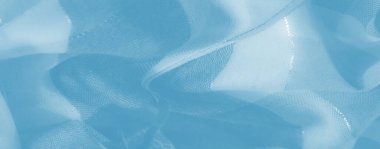 Yumuşak, açık mavi kumaş dokuları hassas yıpranmış ipliklerle sarmaş dolaş. Tekstil katmanlarının dinamik ve ruhani bileşimini oluşturuyor..