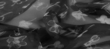 Gri tonda bulanık kumaş tasarımı, yumuşak çiçek aksanlı. Akan kumaşın üzerindeki ışık etkileşimi şeffaf ve zarif dokusunu vurgular..