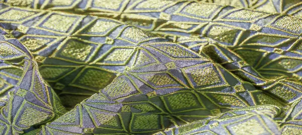 Altın aksanlı, katlanmış yeşil ve mavi kumaşın bulanık görüntüsü. Elmas şekilleri görsel olarak dinamik ve dokulu bir desen oluşturur..