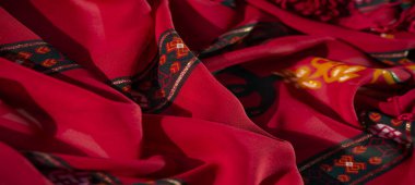 Kırmızı, turuncu ve yeşil tonlarda karmaşık çiçekli ve geometrik desenli bulanık kumaş. Detaylar dokuyu ve sanatçılığı vurgular, yaratıcı tasarımlar için idealdir..