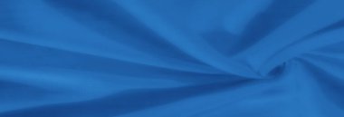 Bulanık, yumuşak kıvrımlarda parlayan parlak mavi kumaşın dinamik bir görüntüsü. Işık ve gölgenin etkileşimi malzemelerin pürüzsüzlüğünü ve zengin mavi tonunu artırır