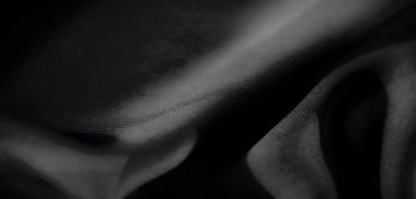 Bulanık, yumuşak, ipeksi dokusunu vurgulayan pürüzsüz kıvrımlı, zarif siyah kumaş. Işık ve gölge etkileşimi lüks bir görünüm yaratır..