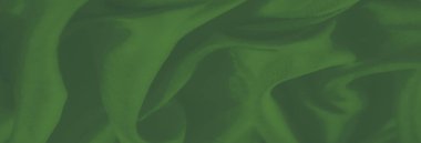 Üst üste binen yeşil kumaş katmanları ve desenli bir kaplama. Yumuşak kıvrımlar ve kıvrımlar materyalin hassas doğasını vurgular..