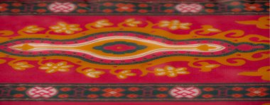 Bulanık kırmızı ve turuncu tekstil simetrik çiçek desenleri ve narin altın aksanlar içeriyor. Kompozisyona zarafet ve enerji katıyor..