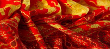 Görüntü kırmızısı kumaş zarif altın filler ve çiçek desenleriyle süslenmiş, tasarım ve dekorasyon projeleri için lüks ve şenlikli bir cazibe sunuyor..