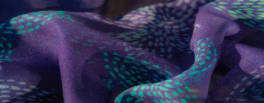 Karmaşık turkuaz desenli yumuşak mor bir kumaş. Işık ve dokuyu vurgulamak için sanatsal olarak katlanmış. Renkler kusursuz bir şekilde karışıyor.